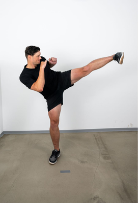 Mann in sportlicher Kleidung führt in Kampfstellung einen hohen Seitwärtskick aus.